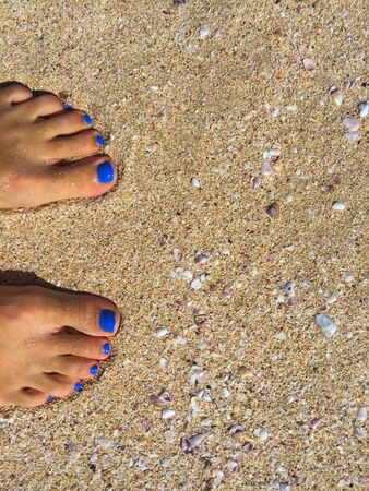 Feet with blue pedicure on the yellow sand beachの写真素材