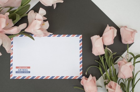 Flat lay composition with air mail envelope and flowers. On envelope - inscription Air Mail in English, French and Spanish. Photo background. Table top view with white and black paper. Floral decorの写真素材