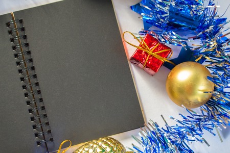 Christmas or New year flat composition. Blue sparkling ribbon wreath. Fir tree ornament. Black paper notebook with blank page. Seasonal decor macro photo for greeting message. Festive backgroundの写真素材