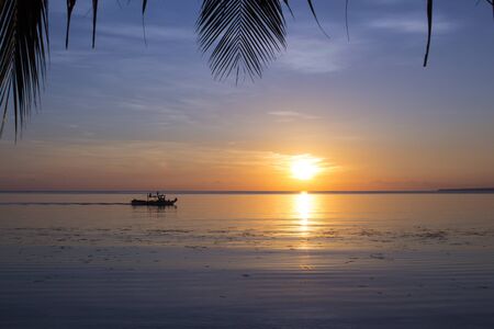 Sea sunset with palm leaves. Idyllic tropical lagoon with a boat. Exotic beach view to orange...