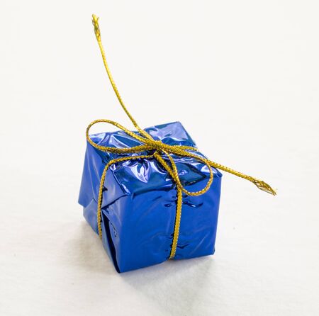 Blue wrapped gift on white background closeup. Christmas gift box in foliage wrapping with gold thread bow. New year fir tree ornament. Winter holiday symbol isolated. Christmas season decor isolateの写真素材