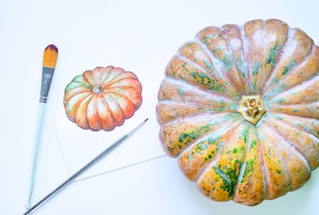 Pumpkin image watercolor painting. Pumpkin vegetable and artwork flat lay composition on table. White work desk with watercolor paintings and brushes. Artist workplace with art supplies and pumpkinの写真素材