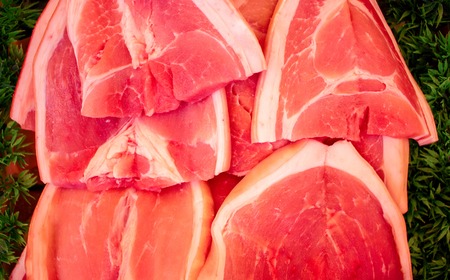 Red meat on a green background. Tasty fresh meat sliced on supermarket display. Protein nutrition or cooking ingredient. Beef or pork red meat. Raw meat closeup photo for recipe illustration or bannerの写真素材