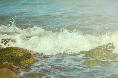Sea surface with white wave over beach stones. Seashore under sun toned photo. Seaside vintage...