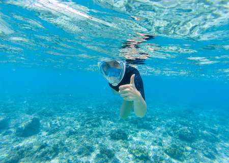 Woman snorkeling in turquoise sea water. Snorkel shows thumb in full face mask. Beautiful girl swims in sea. Underwater photo of oceanic landscape. Seaside adventure. Summer water sport in tropic seaの写真素材