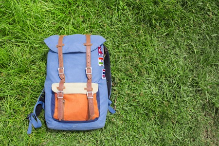 Hipster backpack on summer green grass. Summer travel background photo. Sunny grass lawn with blue backpack. Hipster outdoor banner template with text place. Nomadic lifestyle. Holiday in countrysideの写真素材