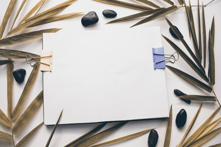 Blank page of notepad with bamboo leaf and beach pebble. White drawing album vintage toned photo. Sepia colored leaf. Autumn season banner template. Yellow leaf and pebbles flat lay. Sketchbook mockupの写真素材