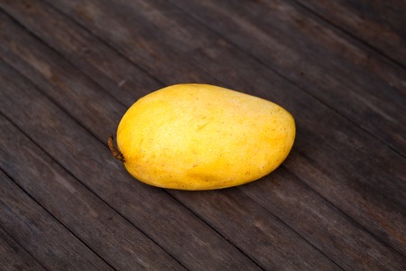 Whole yellow mango on wooden background. Tropical fruit mango on fruit market table. Mango on rustic timber. Whole ripe tropical fruit for juice or dessert. Sweet natural food. Tropic garden harvestの写真素材