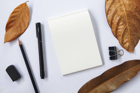 Autumn season workspace top view. Black pen and pencil. White paper of notepad blank page. Yellow...