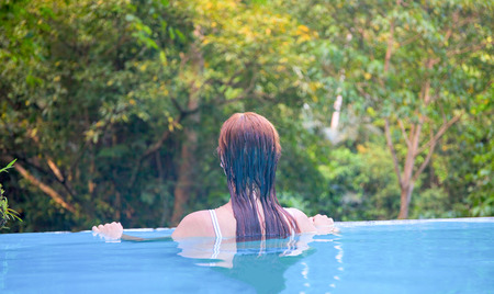 Relaxed woman in blue swimming pool. Girl in open swimming pool. Summer vacation vintage toned photo. Tropical jungle hotel scene. Exotic holiday. Outdoor swimming pool with natural viewの写真素材
