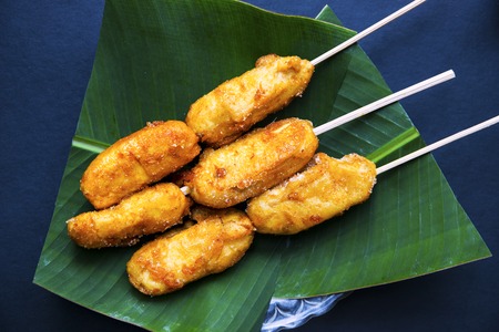 Fried banana on banana leaf plate. Fried fruit asian dessert. Golden bananas on sticks served for food. Tropical resort breakfast. Exotic island lifestyle. Tropical dessert. South Asia snack flat layの写真素材