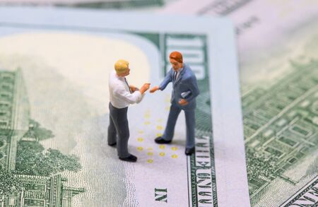 Businessmen figurines shaking hands on cash. Tiny businessmen models on money background. Finance or economic growth concept. Making profitable deal. Buy and sell transactions for cash moneyの写真素材