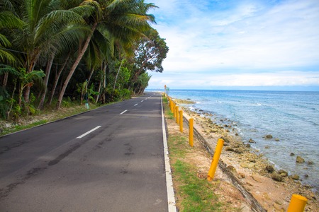 Empty coastal road by the sea. Tropical island holiday travel. Sunny road in tropical nature. Summer travel on car or motorbike. Philippines transportation infrastructure. Blue sky and coco palm treesの写真素材