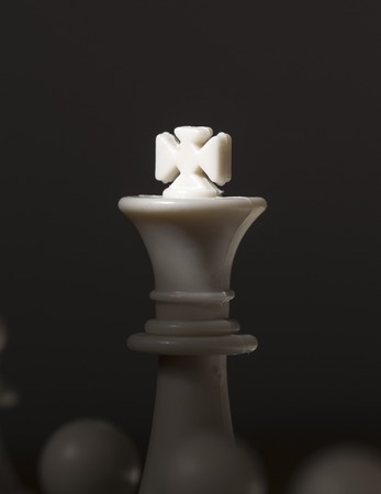 Chess figure king with light on crown. White chess king. Chessmate victory concept photo. White king between pawns. Chessboard game. Black and white vertical image of checkmate. Leadership metaphorの写真素材