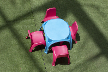 Plastic table and chairs on green carpet, children's playground in a shopping mall. Green carpet with toy table and chairs. Children playground with lunch table. Plastic furniture for kids in sunlightの写真素材
