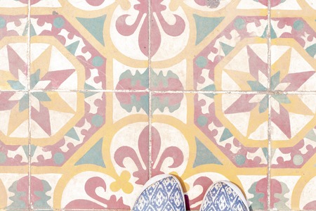 Woman feet on colorful tiles on asian street. Oriental travel banner template with text place. Pastel color tiles of outdoor paving. South Asia travel in comfortable shoes. Vintage tile floor top viewの写真素材