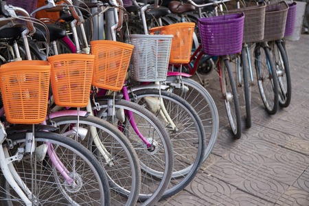Modern urban bicycles with baskets. Bikes for rent in asian city. Urban transport of summer town. Vintage bicycles parking on tile paving street. Transport in Asia. Modern city two wheel vehicleの写真素材