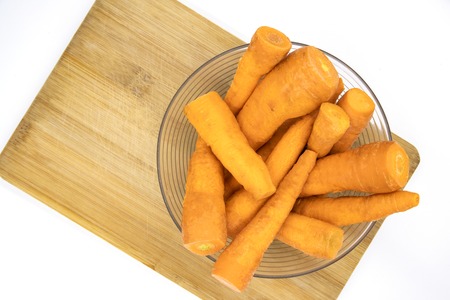 Fresh orange carrot in glass bowl top view photo. Many carrots cleaned for cooking. Healthy dish ingredient. Small carrots on wooden cutting board. Summer vegetable for healthy diet. Food for sun tanの写真素材