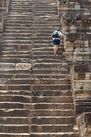 Man tourist climbs the high stair of ancient temple. Endless steps of ancient buddhist temple in Angkor Wat. Tourist climbing historical building. Sightseeing in Cambodia. Ancient place of interestの写真素材