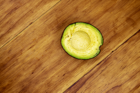 Green avocado half on wooden table, top view photo. Single avocado top view photo. Cut avocado vegetable on wooden board. Exotic fruit with delicious taste. Fresh vegetable for recipe. Healthy foodの写真素材
