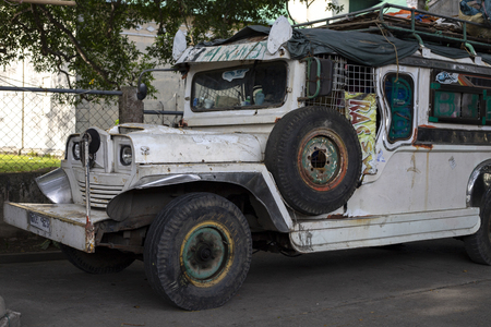 Dumaguete, the Philippines - 27 July 2018: White vintage jeep on street. Street scene in Philippines. Traditional symbolic military car. Vintage jeep car. Filipino iconic public transport. Old jeepneyのeditorial素材