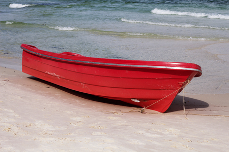 Empty red boat on white sand beach by blue sea water. Seaside activity kayaking. Marine guard boat. Beach day scene. Red boat of coast guardian. Tropical seashore scenery. Exotic island vacationの写真素材