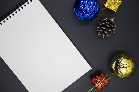 Christmas tree decor and blank notebook flat lay on black background. Christmas or New Year mockup. Winter holiday banner template with sketchbook. Blue and golden Christmas fir tree toys top viewの写真素材