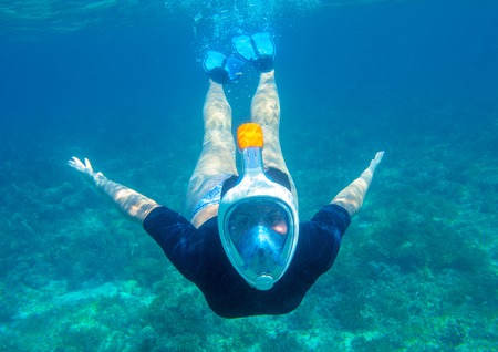 Young woman diving underwater photo. Snorkel in coral reef of tropical sea. Young girl in full-face...