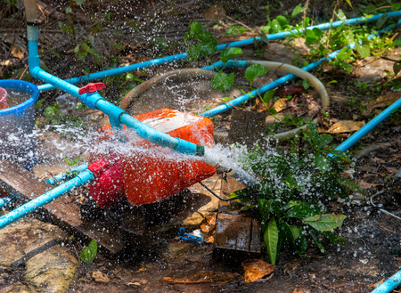 Breakthrough water pipe. Broken water supply. Fresh water recourse waste. South Asia water supply problem. Blue pipes and orange tank mechanism. Splash from pipeline. Broken plumbing in summer gardenの写真素材