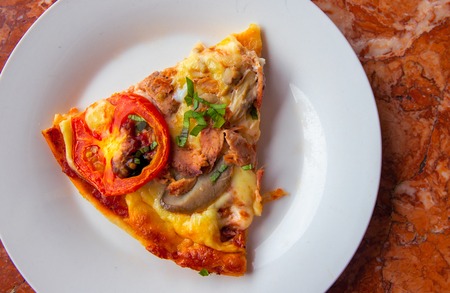 Piece of pizza with tomato, herbs and cheese on white plate. Pizza slice on stone table top view....
