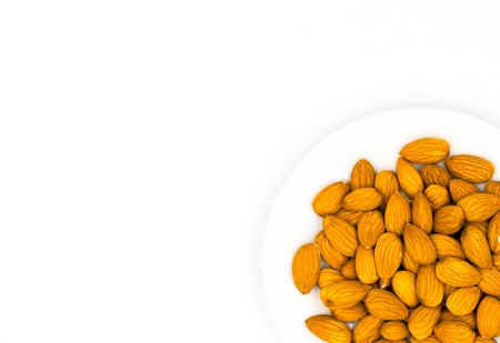 Almond on plate on white background with place for text, top view photo. Tasty healthy snack. Scattered nut on table. Organic food rustic banner template. Natural nut flat lay. Whole almond flat layの写真素材