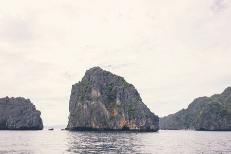 Rocky island in sea, neutral from tropical vacation. Retro travel card. Unusual tropical landscape with sea and mountain. Summer travel in Asia. Rain season view. Still seaside natural sceneの写真素材