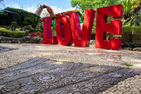 Love red letters in green tropical park, outdoor decor photo. Huge letters of Love inscription. Selfie or photo spot idea. Public park attraction. Love standing letters for wedding photographyの写真素材