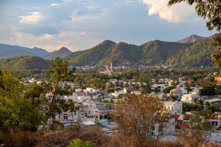Nha Trang, Vietnam - 24 Jul 2019: City view with buildings and distant mountains in sunset light. Peaceful asian city panorama. South Asia travel photo. Mountains and sky landscape. Small white housesのeditorial素材