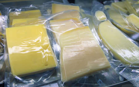 Stock of yellow cheese in vacuum packaging. Cheese slices in grocery shop. Fresh goat cheese for...