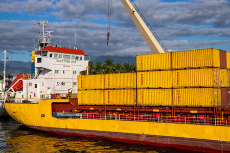 Dumaguete, the Philippines - 10 Mar 2020: yellow cargo ship in port, with containers loaded. Maritime shipping and delivery service. Goods cargo transportation. Nautical vessel with container freightのeditorial素材