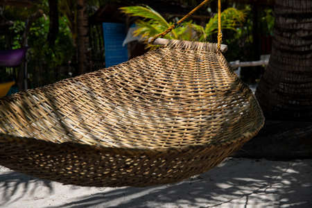 Braided hammock in palm leaf shadow on beach. Empty hammock of abandoned luxury resort. No tourist in hotel concept. COVID-19 pandemic impact on tourism industry. Summer vacation on tropical islandの写真素材