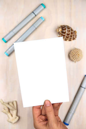 Vertical postcard mockup in female hand on wooden table background. Blank postcard in hand. Empty...