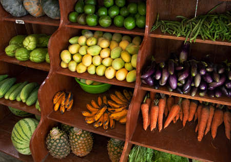 Vegetable and fruit on shelf in store. Healthy vegetarian eating raw ingredient for cook in food shop. Tropical fruit mango for sale. Organic shop display with eggplant, pineapple, banana and carrotの写真素材