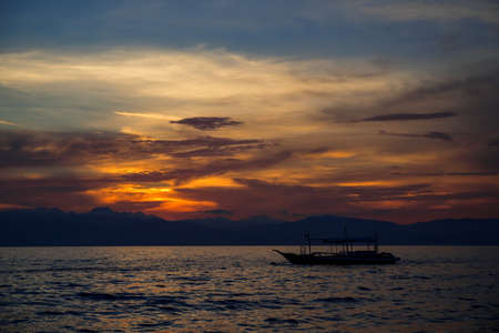 Sunset sea landscape with native boat. Philippines travel photo of beautiful seaside. Early morning seascape sun and cloud. Blue orange scenic sky view. Tropical seaside on sunrise. Summer vacationの写真素材