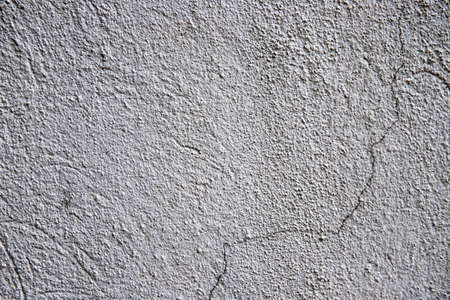 White plaster painted wall with grit and cracks. Cracked wall closeup photo. Architecture detail background. Empty concrete wall. Grungy surface of painted cement. Abstract grainy textureの写真素材