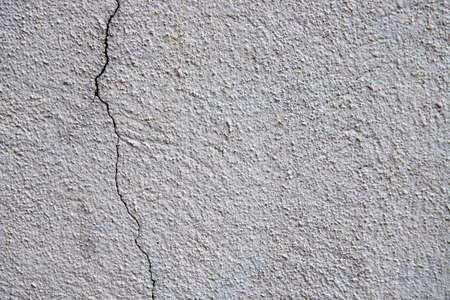 Pale plaster painted wall with grit and cracks. Cracked wall closeup photo. Architecture detail background. Empty concrete wall. Grungy surface of painted cement. Abstract grainy textureの写真素材
