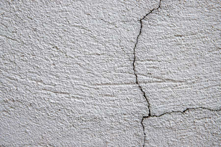White plaster painted wall with cracks. Cracked wall closeup photo. Architecture detail background. Empty concrete wall. Grungy surface of painted cement. Abstract grainy textureの写真素材