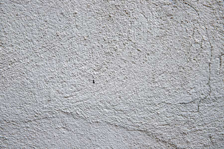 White plaster painted wall with grit and grain. Cracked wall closeup photo. Architecture detail background. Empty concrete wall. Grungy surface of painted cement. Abstract grainy textureの写真素材
