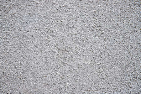 White plaster painted wall with grain and noise. Cracked wall closeup photo. Architecture detail background. Empty concrete wall. Grungy surface of painted cement. Abstract grainy textureの写真素材