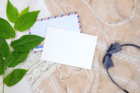 Black card with air mail envelope. Bohemian background with lace dress, headband and sunglasses. Summer vacation top view composition. White paper postcard mockup. Summer travel card with holiday wearの写真素材