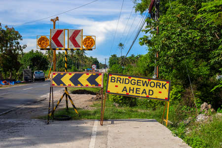 Bridgework ahead yellow sign on road construction site. South Asia economical development concept. Road construction in the Philippines. Warning sign on rad. Tropical country travel or road tripの写真素材