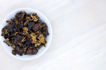 Dried black mushroom in bowl on wooden table. Wood ear mushroom pile top view photo. Dry mushroom for soup or garnish ingredient. Natural healthy food from chinese market. Asian cuisine dishの写真素材