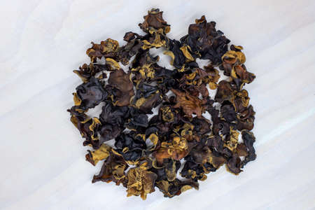 Dried black mushroom on white wooden kitchen table. Wood ear mushroom pile top view photo. Dry mushroom for soup or garnish ingredient. Natural healthy food from chinese market. Asian cuisine dishの写真素材