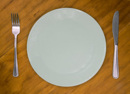 Empty plate with knife and fork on wooden background. Cutlery and plate on wooden backdrop. Photo of an empty plate for the restaurant menu. The concept of waiting for food.の写真素材